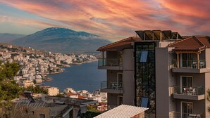 A multi-story building with balconies overlooking a coastal cityscape and a mountain in the background. - Angel Saranda Palace (Sarande)