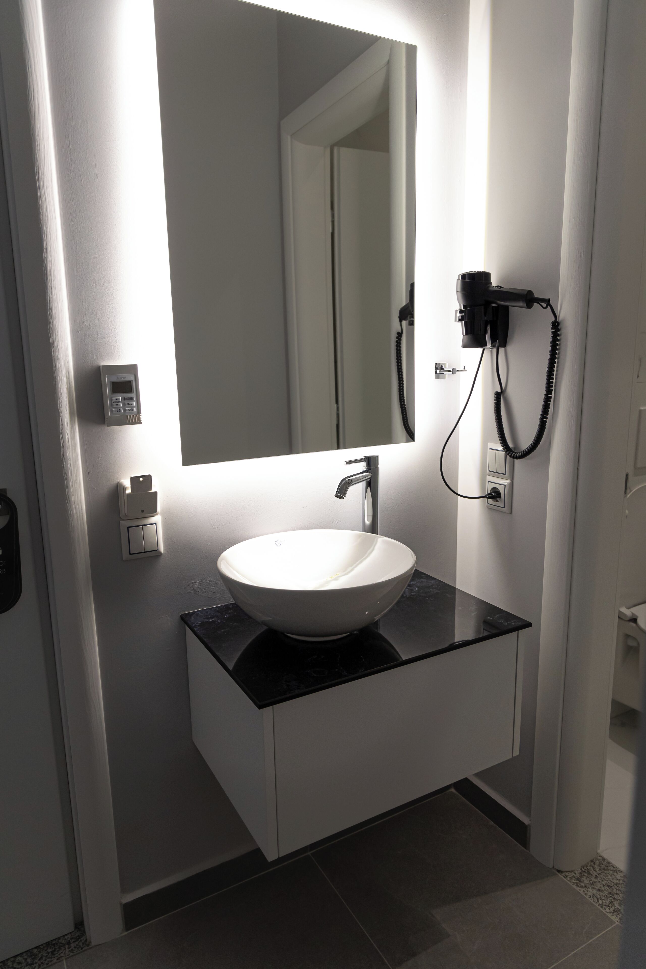Ein modernes Badezimmer mit einem weißen Waschbecken, einer schwarzen Arbeitsplatte und einem großen Spiegel.