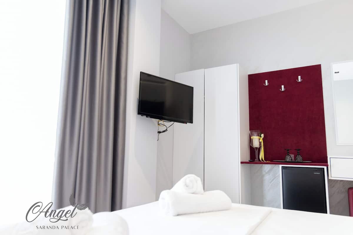 A hotel room with a bed, a TV mounted on the wall, a minibar, and a red accent wall.