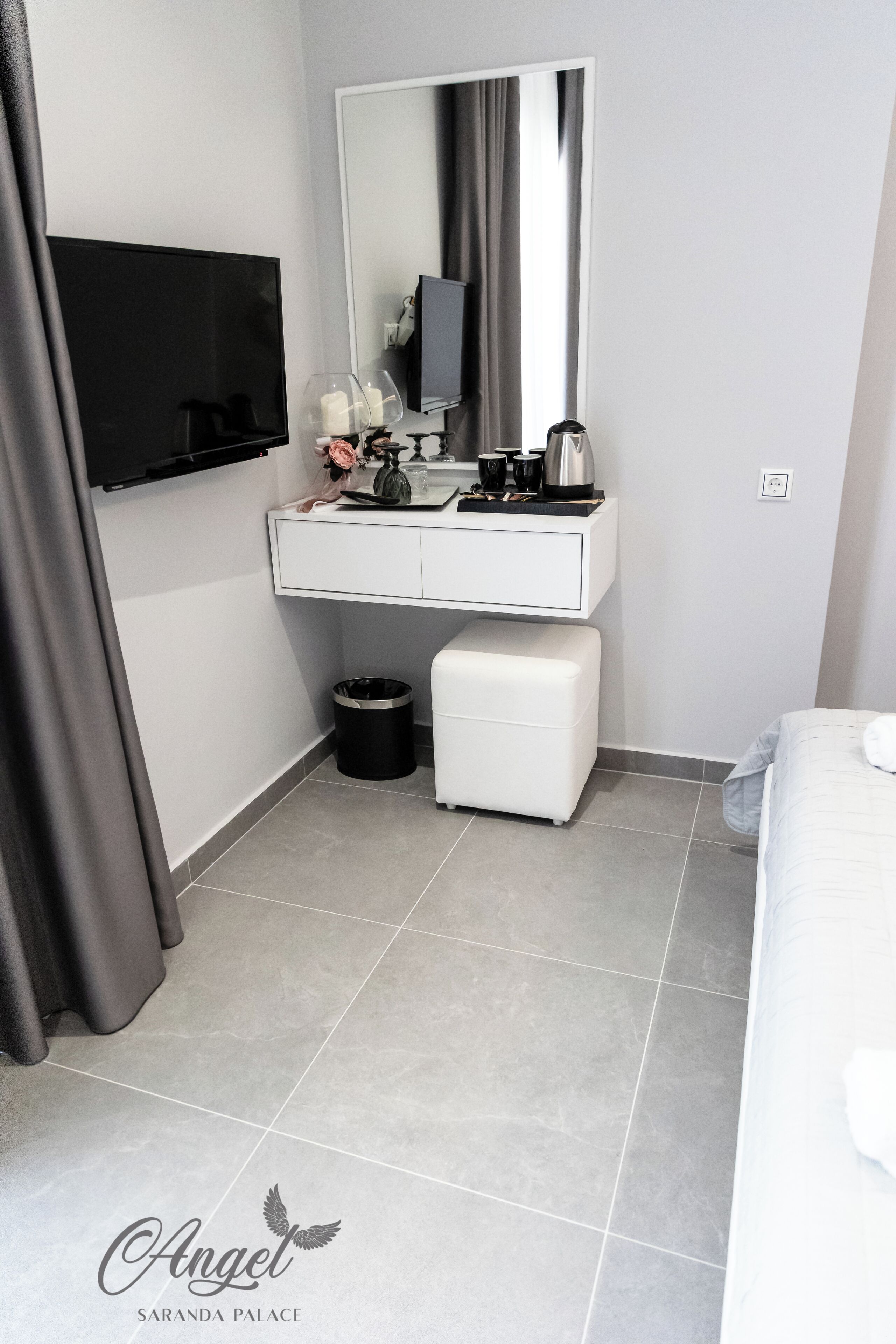 Un baño moderno con tocador blanco, espejo, cubo de basura negro y banco blanco.