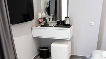 Un baño moderno con tocador blanco, espejo, cubo de basura negro y banco blanco.