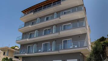 Een meerlaags hotel met balkons, een houten terras op het dak en een stenen muur aan de voet.