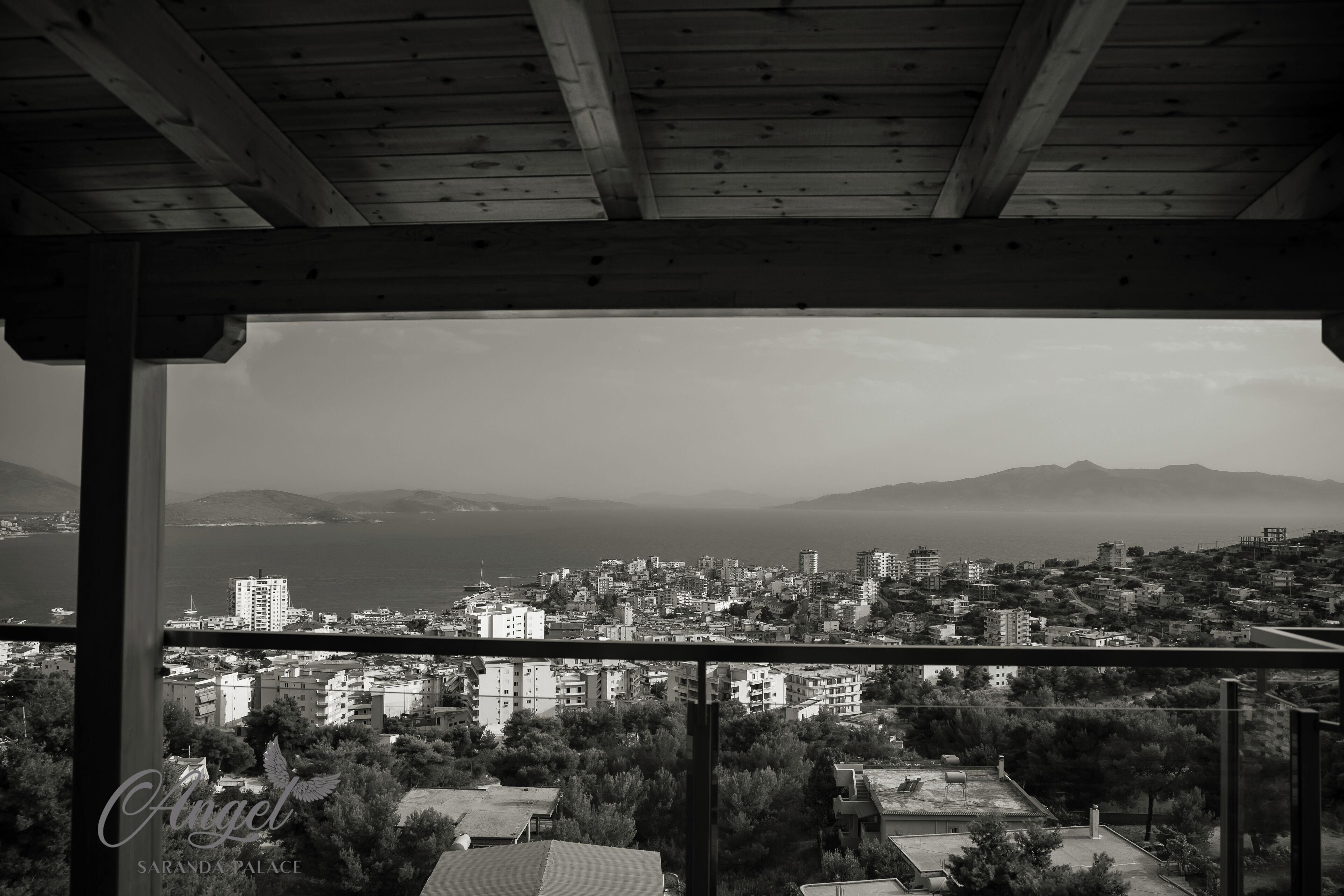 Vista en blanco y negro de un paisaje urbano costero desde un balcón con techo de madera.