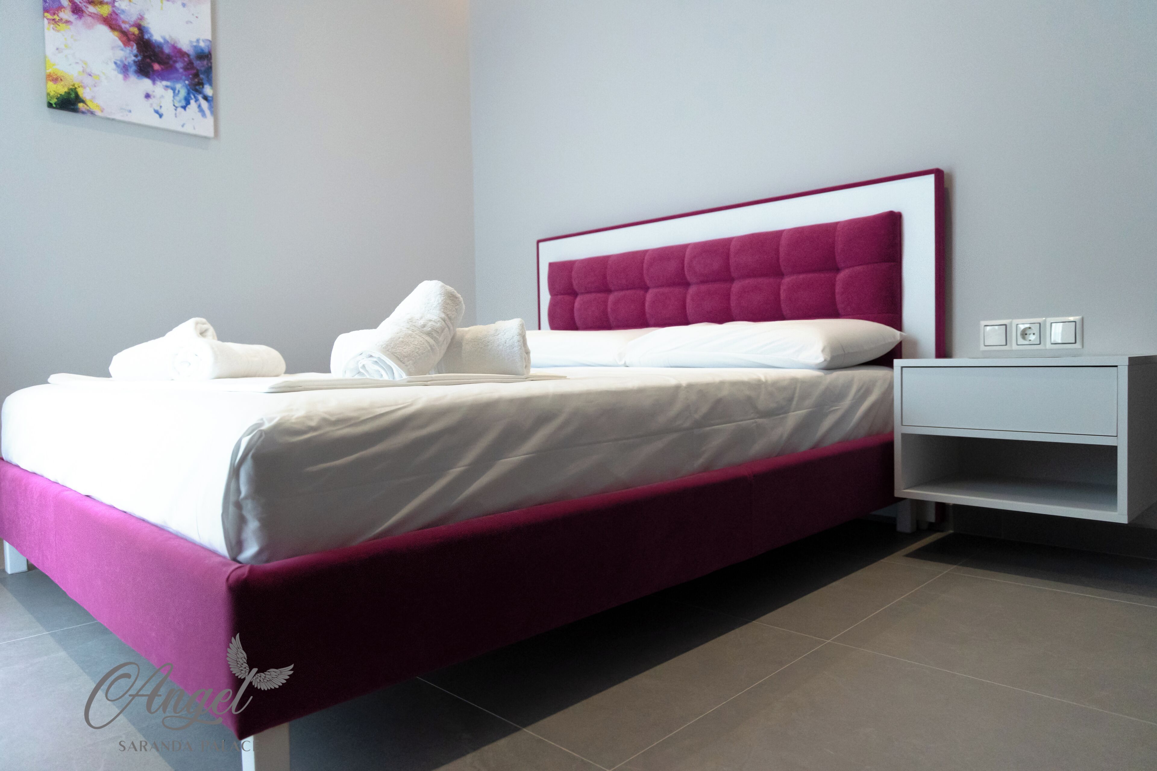 A modern bedroom with a bed, white nightstands, and a colorful abstract painting on the wall.