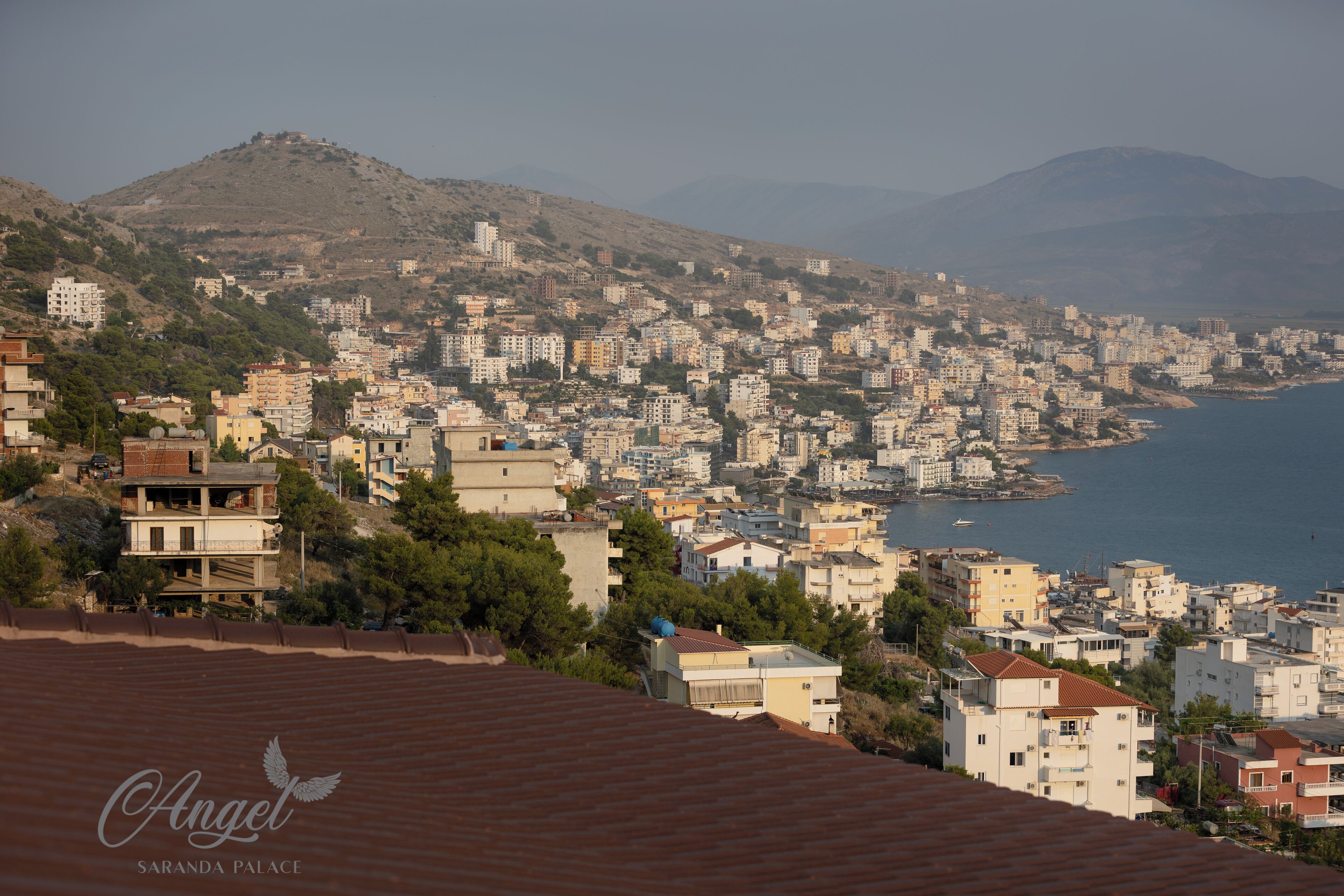 A coastal cityscape with buildings, a hill, and a body of water.