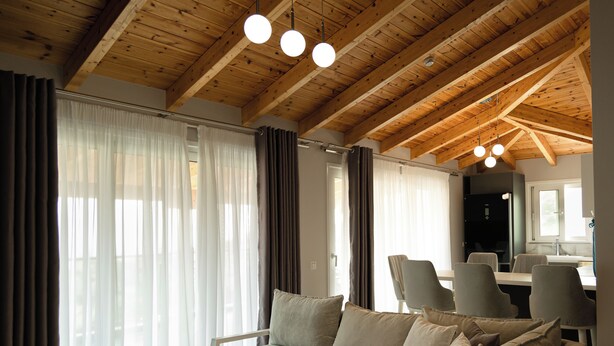 A modern living room with a wooden ceiling, a grey sofa, and a dining area with chairs and a table. - Angel Saranda Palace (Sarande)