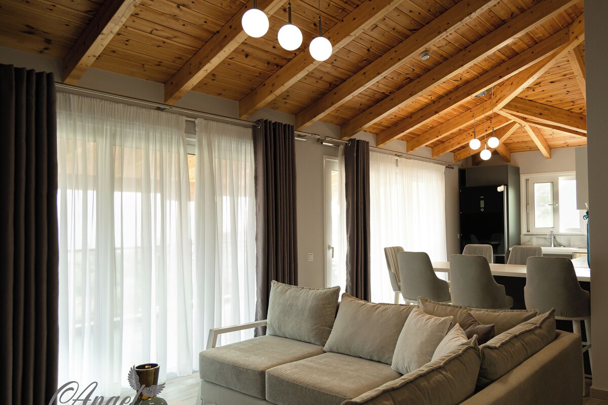 Uma sala de estar moderna com teto de madeira, um sofá cinzento e uma área de jantar com cadeiras e mesa.