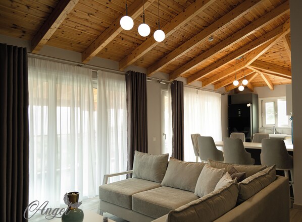 Uma sala de estar moderna com teto de madeira, um sofá cinzento e uma área de jantar com cadeiras e mesa.