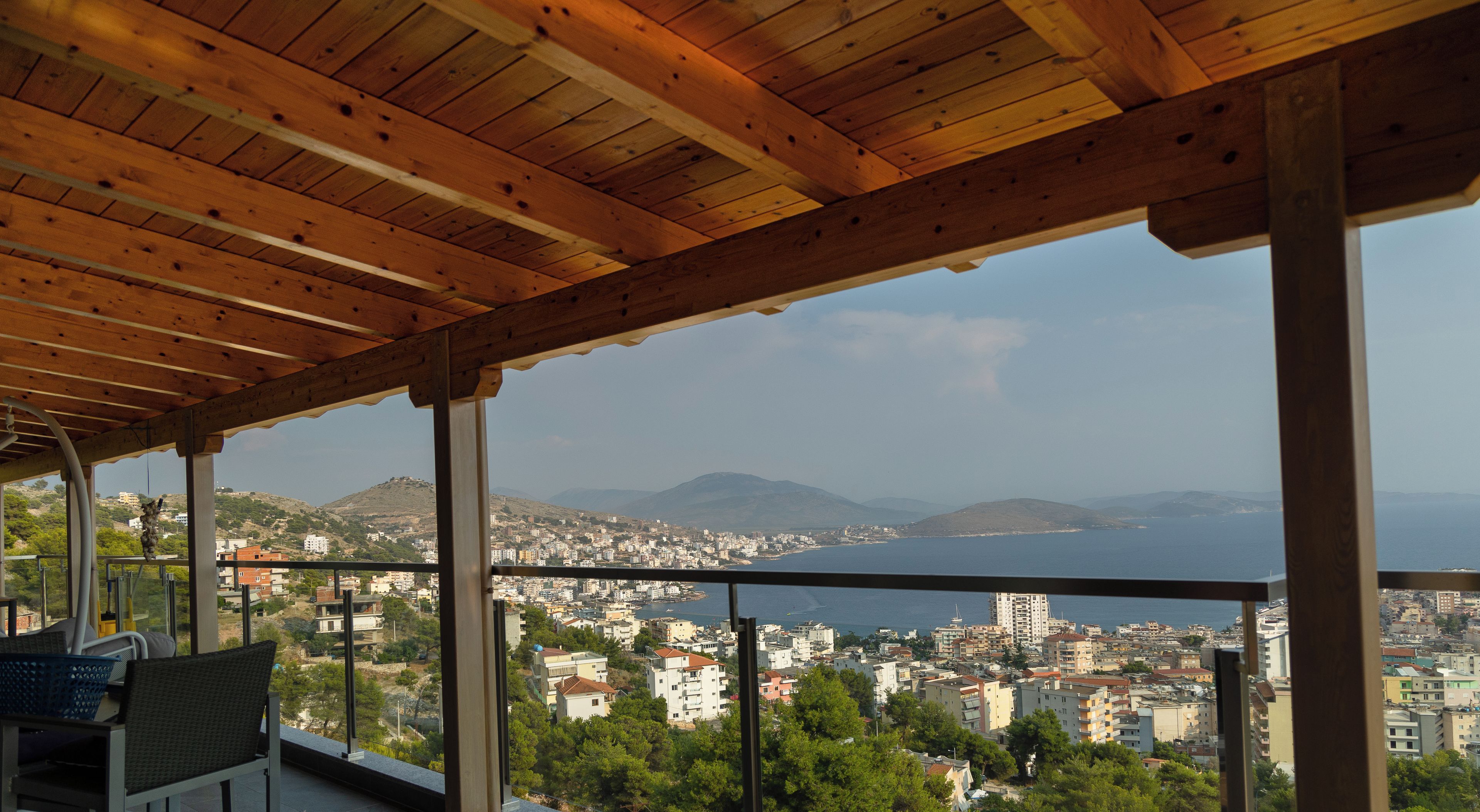 Un balcón con vistas a una ciudad costera, techo de madera y una silla.
