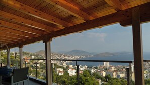 A balcony with a view of a coastal city, wooden ceiling, and a chair. - Angel Saranda Palace (Sarande)