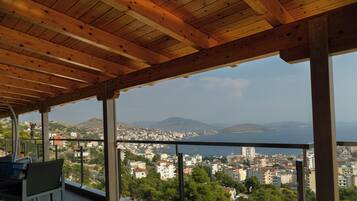 Un balcón con vistas a una ciudad costera, techo de madera y una silla.