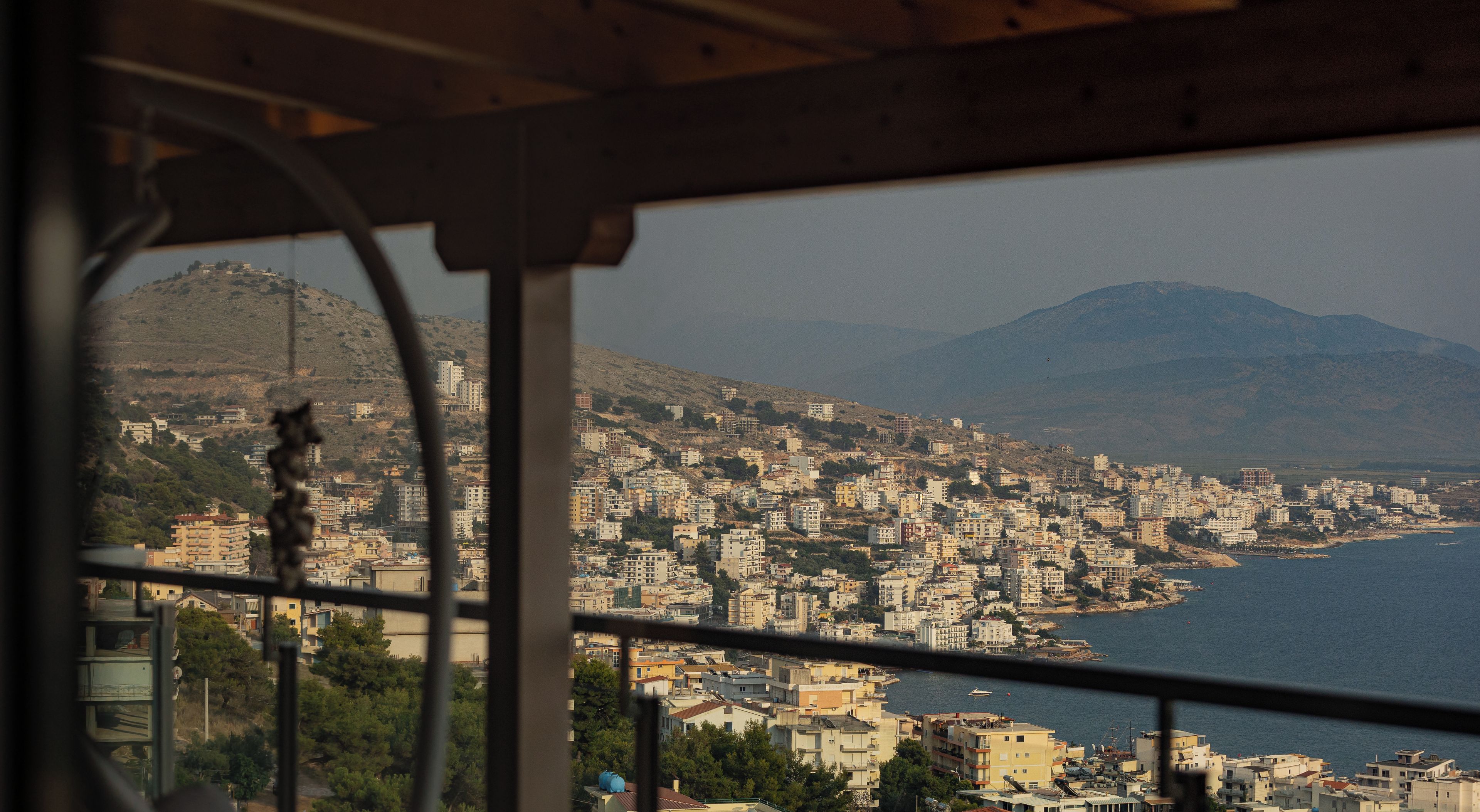A view from a window overlooking a coastal cityscape with buildings and a mountain in the background.
