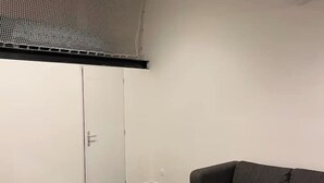 A room with a closed white wardrobe, a dark grey sofa, and a black ceiling vent. - T2 Design - Montpellier Centre (Montpellier)