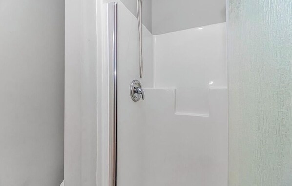 A bathroom with a glass shower enclosure, a white door, and a white wall.