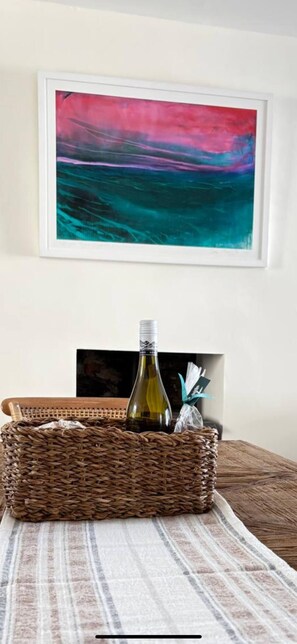 A room with a framed abstract painting, a wicker basket with a bottle and napkins, and a striped rug. - Anchor & Nest - 4 bedroom seaview house in Kinsale (Kinsale)