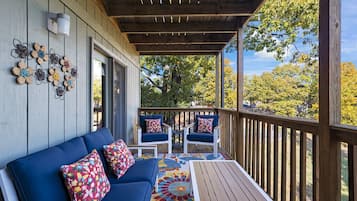 A covered porch with a blue sofa and two chairs, a wooden table, and a colorful rug.
