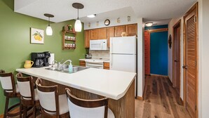 Una cocina con una isla central, armarios de madera, un microondas y un refrigerador. Hay taburetes de bar y una cafetera en la isla.