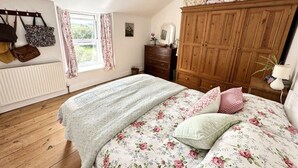 A bedroom with a wooden wardrobe, a bed with floral bedding, a radiator, and a window with curtains.