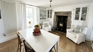 A cozy living room with a stone fireplace, white furniture, and a dining table with fruit.