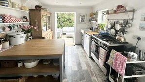 A kitchen with a wooden countertop, a stove, and various kitchen utensils. There is a window providing natural light and a view of greenery outside.