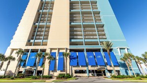 A multi-story hotel with a beige and blue facade, palm trees, and blue awnings. - Coastal Escape West - Unit 506, beach service inc., 1 mile West of Pier Park (Panama City Beach)