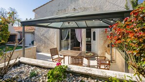 Un patio cubierto con una mesa y sillas, un sendero de piedra y un edificio con fachada blanca.