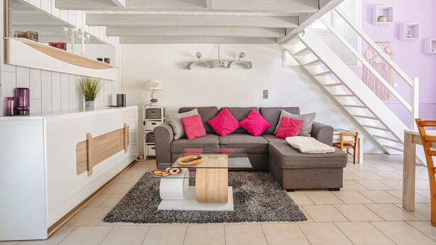Una sala de estar moderna con una mesa de centro de vidrio, un sofá gris y una escalera con barandillas blancas.