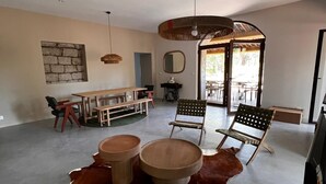 Amplia sala de estar con una gran mesa de comedor de madera, dos mesas redondas de centro y un tapete de cuero de vaca. Se observan varias sillas y un colgante.