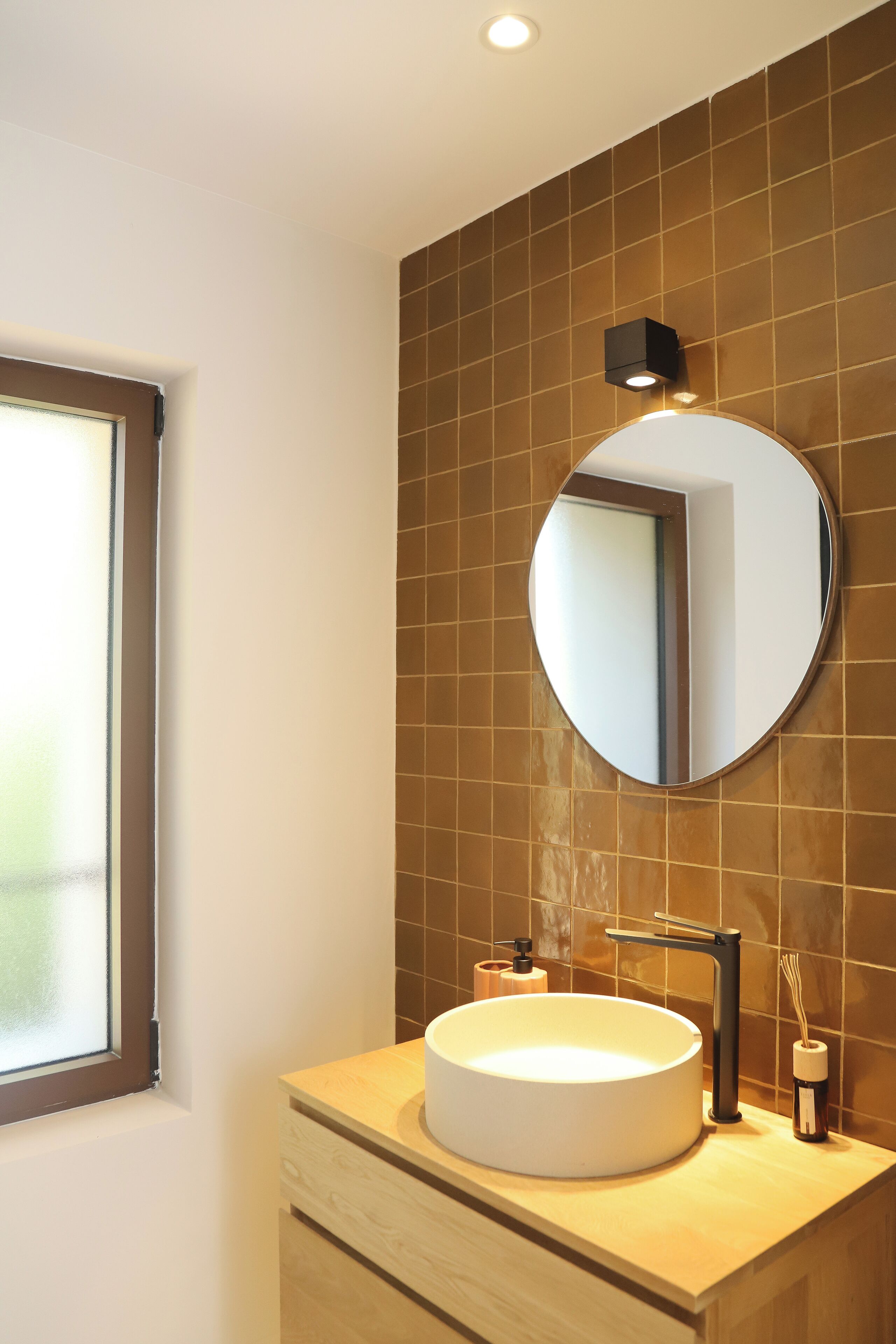 A modern bathroom with a round mirror, a white sink, and a window.