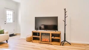 A modern living room with a flat-screen TV on a wooden stand, a coat rack, and a white door.