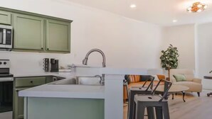 A modern kitchen with green cabinets, a central island, and a dining area with a sofa and bar stools.
