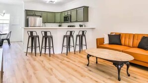 A modern kitchen with green cabinets, a central island with bar stools, and a wooden dining table.