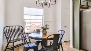 A dining area with a round table, four chairs, a chandelier, and a view of the outside through a window.