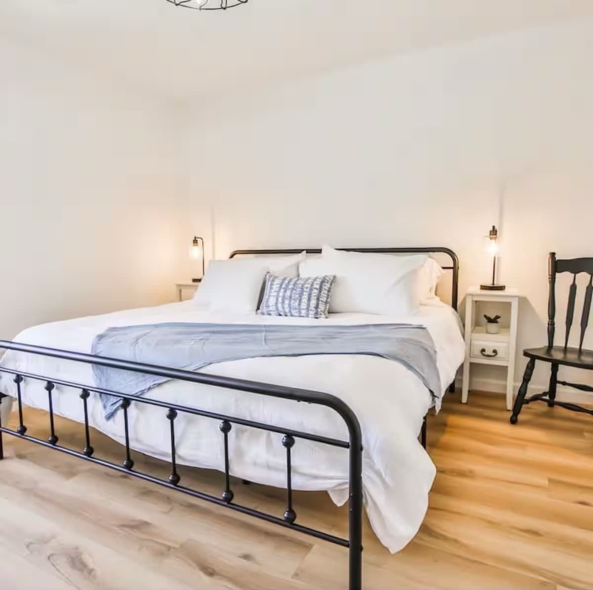 Een enkel bed met een metalen frame, wit beddengoed, een nachtkastje met een lamp en een stoel.