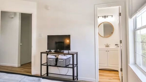 A bedroom with a bed, a TV on a stand, a wardrobe, and a window.