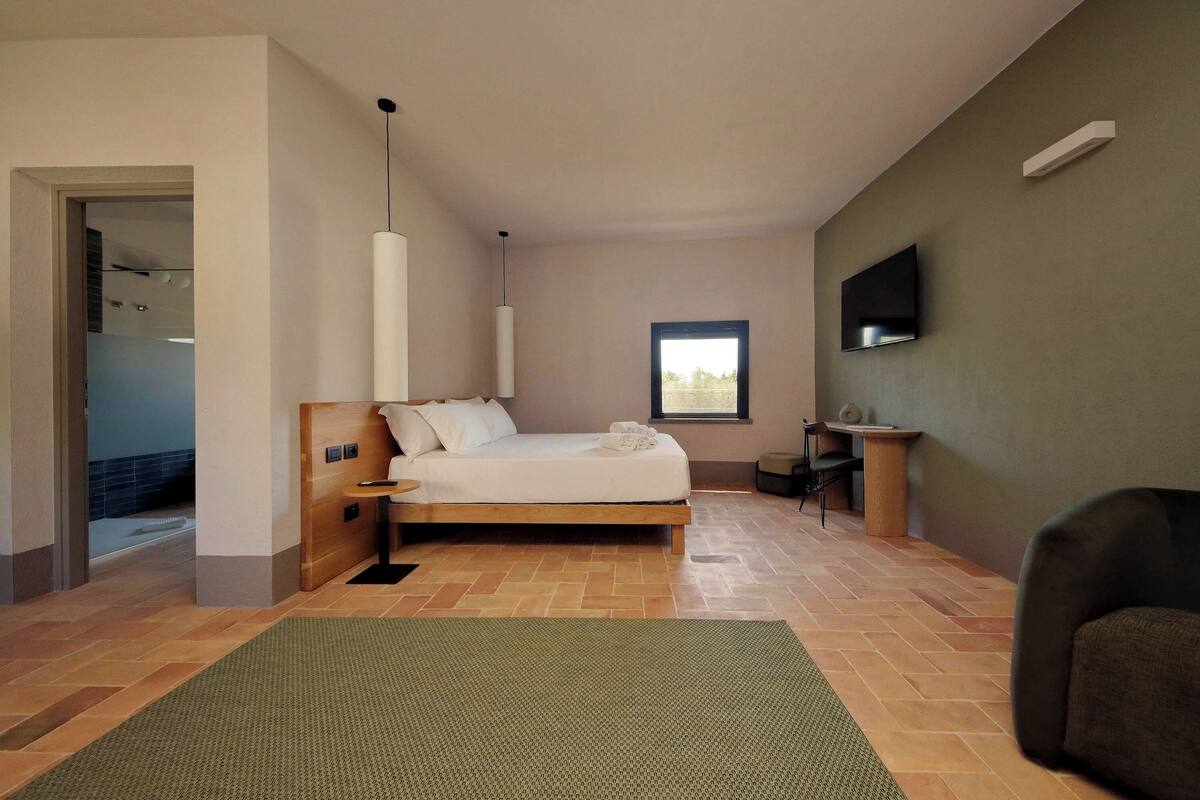 Une chambre à coucher moderne, avec un lit, un téléviseur fixé au mur et une fenêtre laissant entrer la lumière naturelle.