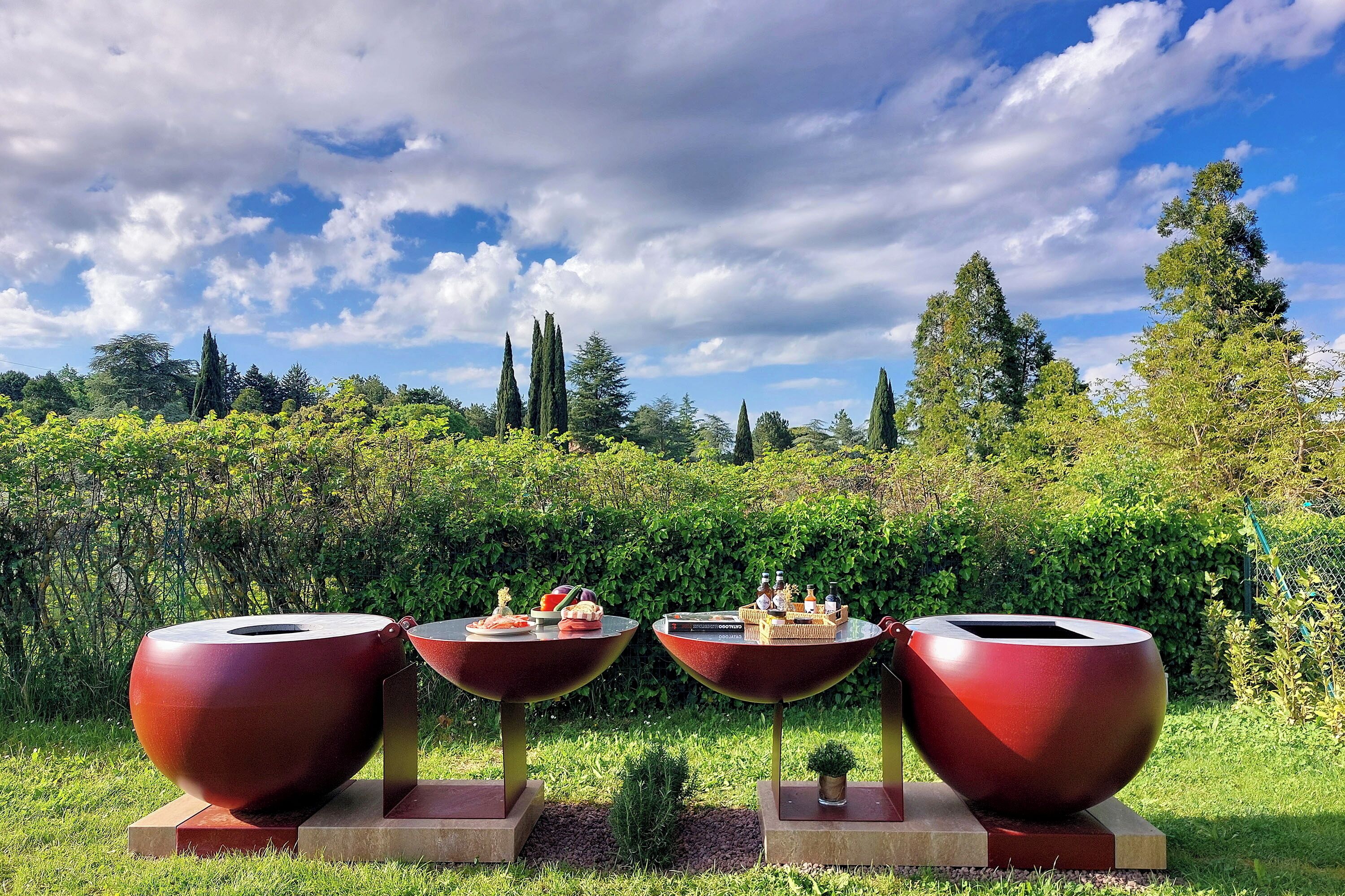 Tres estructuras grandes, rojas y en forma de cuenco con mesas en un jardín.
