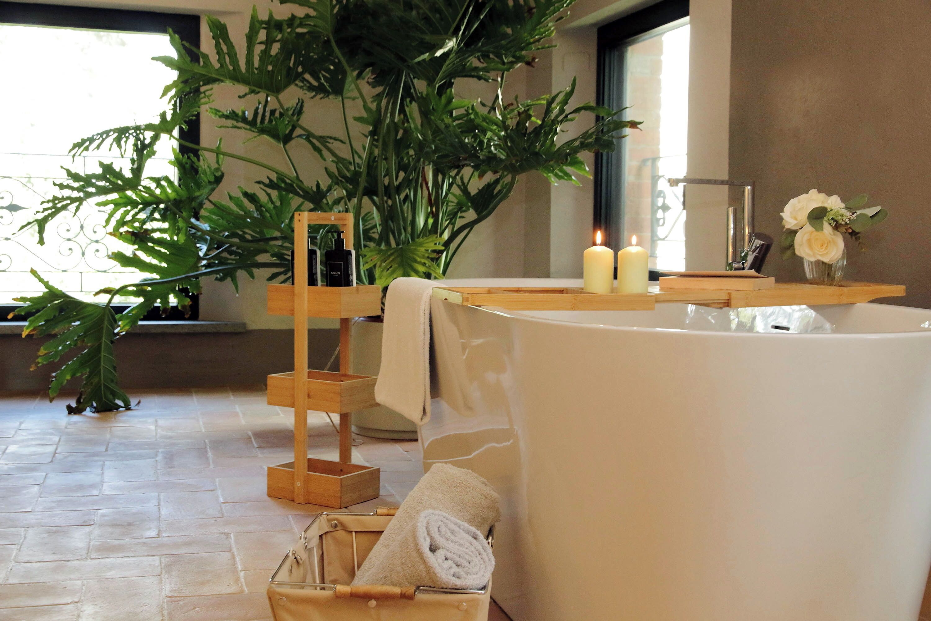 Un baño con bañera, una mesita de madera con velas, una planta en maceta y un cesto para toallas.