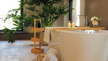 Un baño con bañera, una mesita de madera con velas, una planta en maceta y un cesto para toallas.