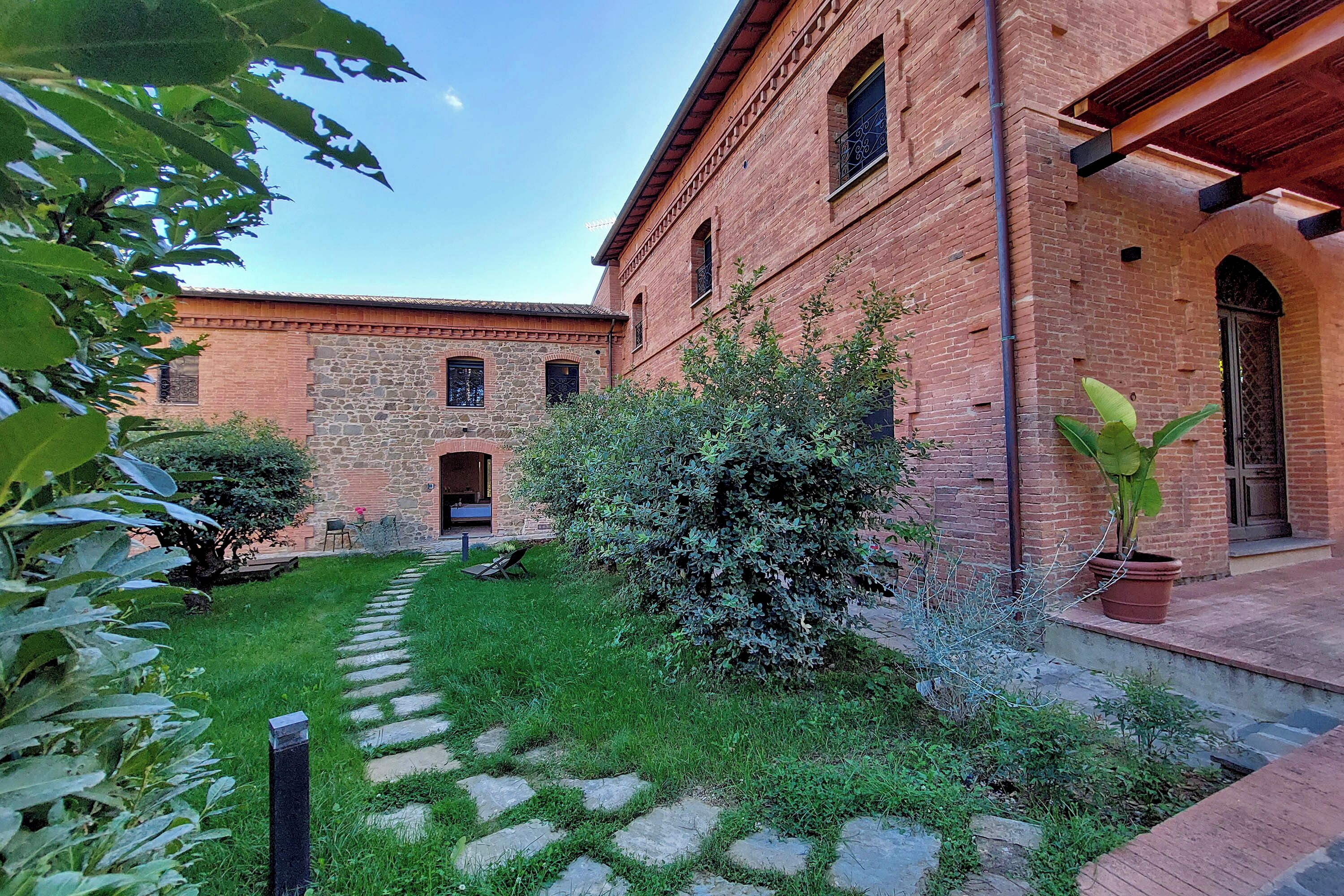 A courtyard with a stone pathway, a brick building with arched windows, and a potted plant.