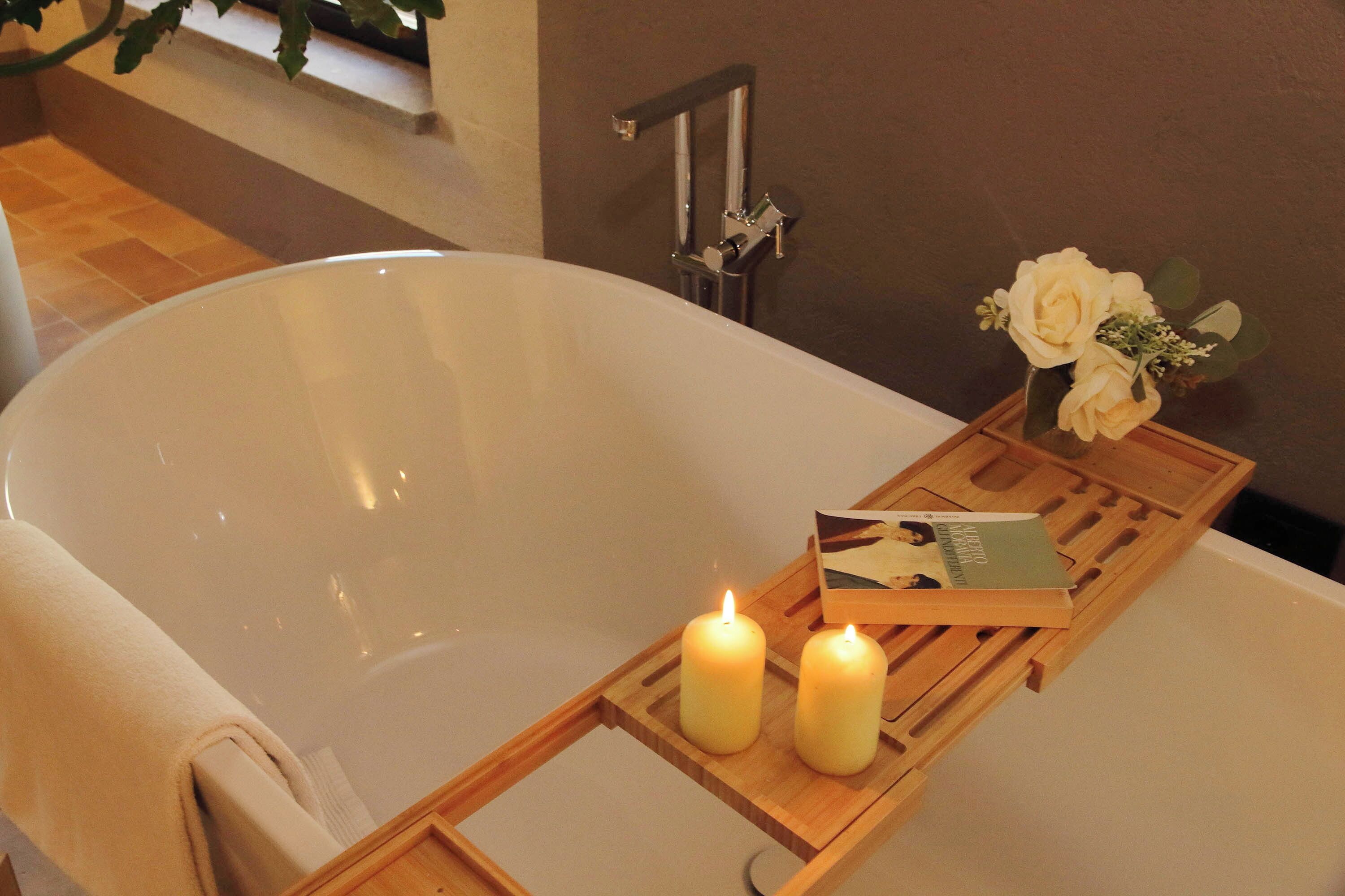 Une baignoire avec deux bougies allumées et un livre posé sur un plateau en bois.