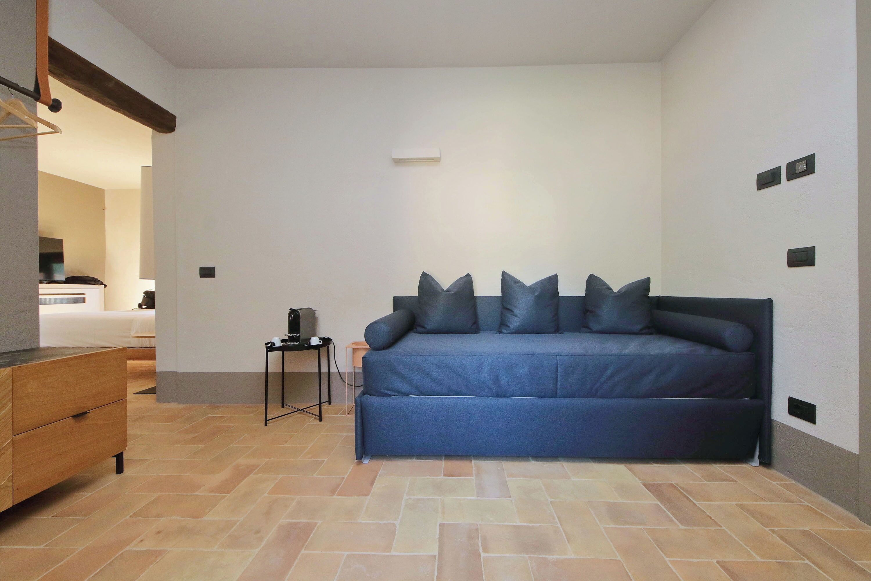 Una habitación con un sofá azul, un aparador de madera y una mesita de noche con una lámpara.
