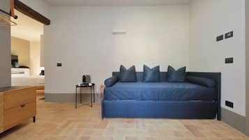 Una habitación con un sofá azul, un aparador de madera y una mesita de noche con una lámpara.