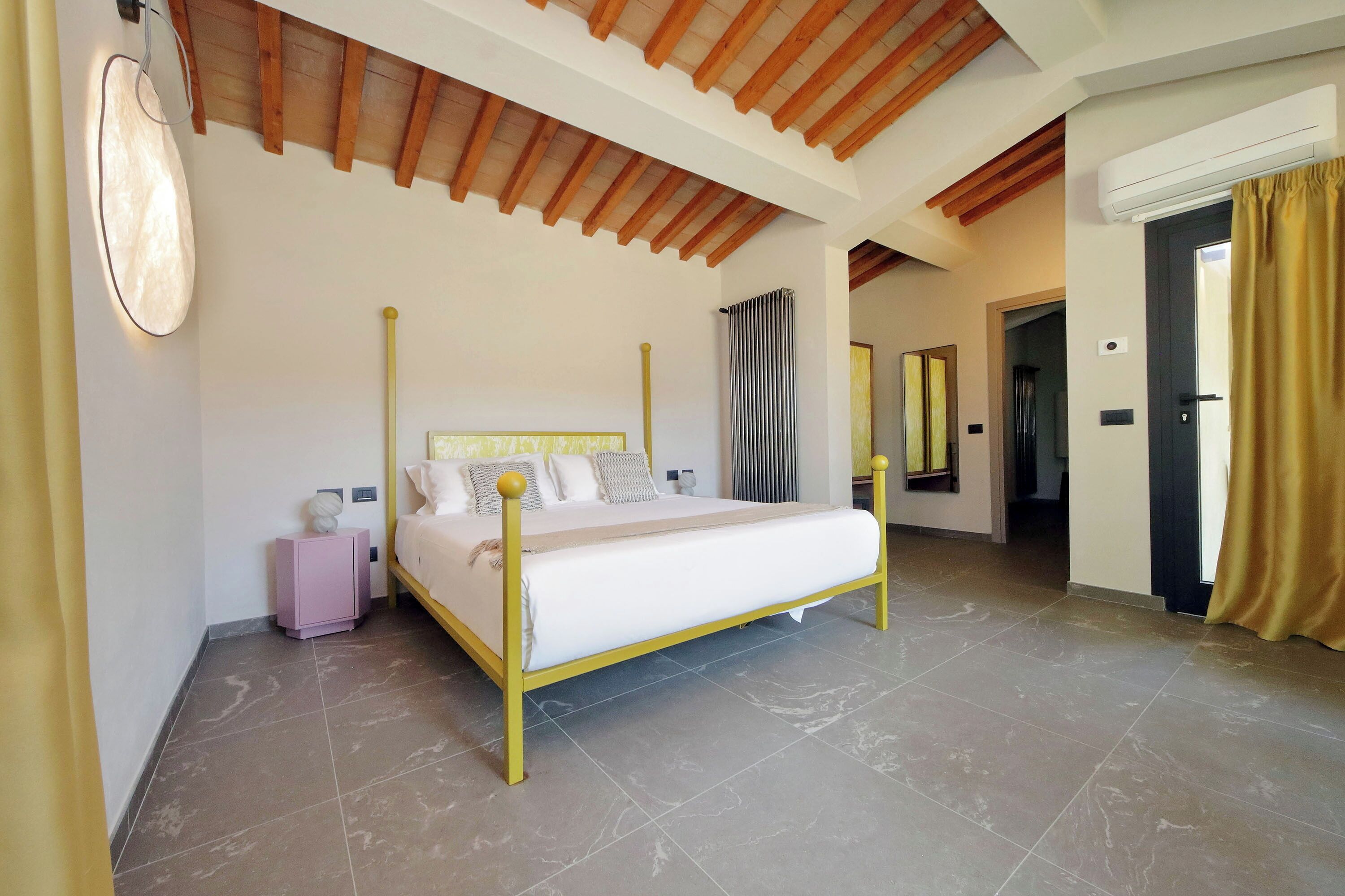 A bedroom with a four-poster bed, a bedside table, a nightstand, a wall-mounted light, and a radiator.