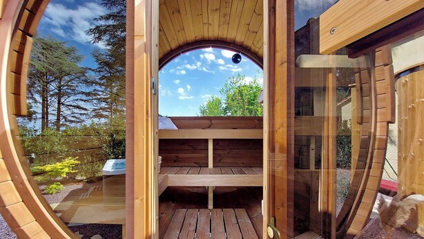 Une structure en bois dotée d’une fenêtre circulaire, d’une terrasse en bois et offrant une vue sur les arbres et le ciel.