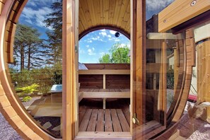 Een houten constructie met een rond raam, een houten terras en uitzicht op bomen en lucht.