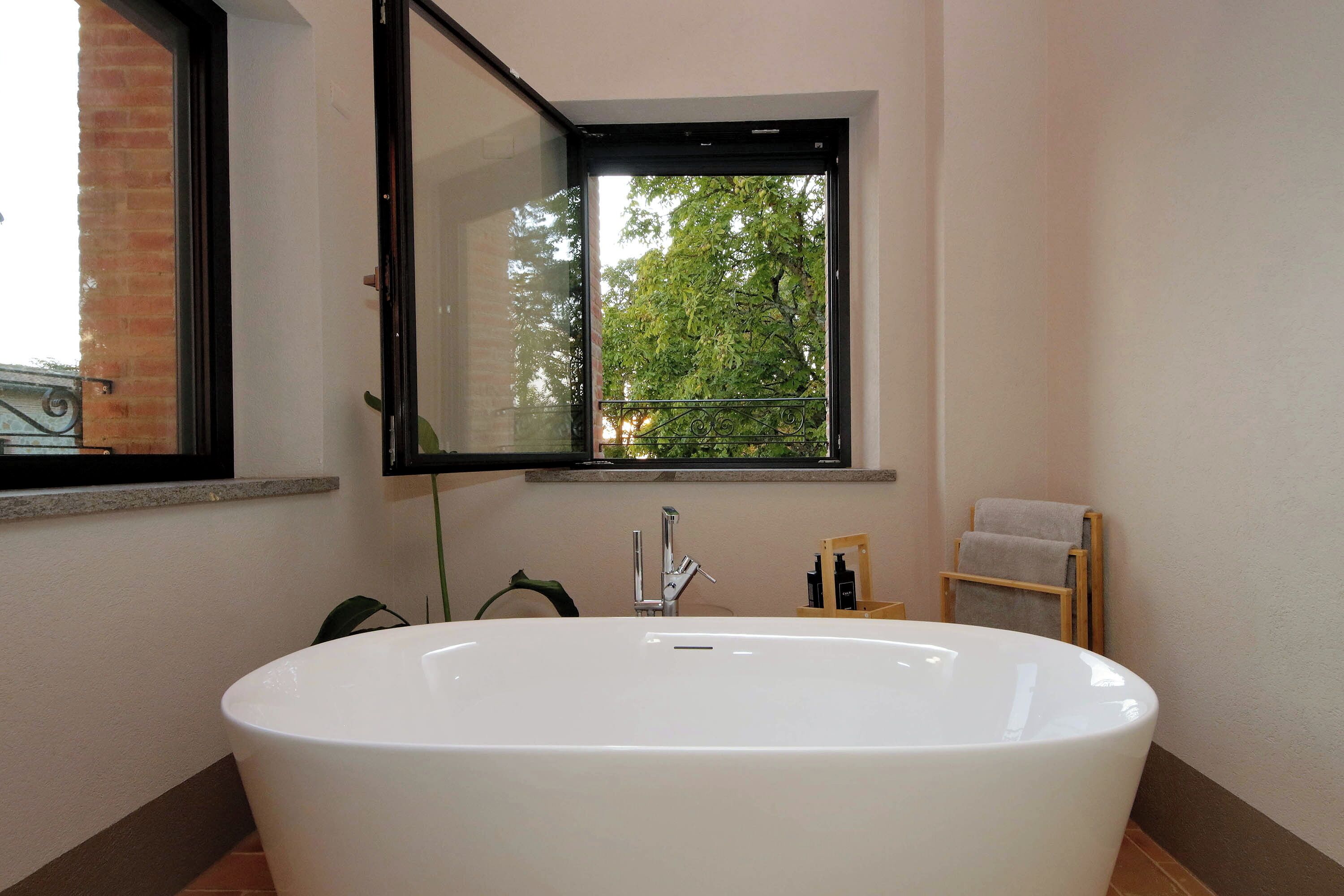 Ein Badezimmer mit einer großen weißen Badewanne, einem Fenster mit Blick auf Bäume und einem Handtuchhalter.
