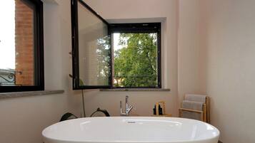 Ein Badezimmer mit einer großen weißen Badewanne, einem Fenster mit Blick auf Bäume und einem Handtuchhalter.