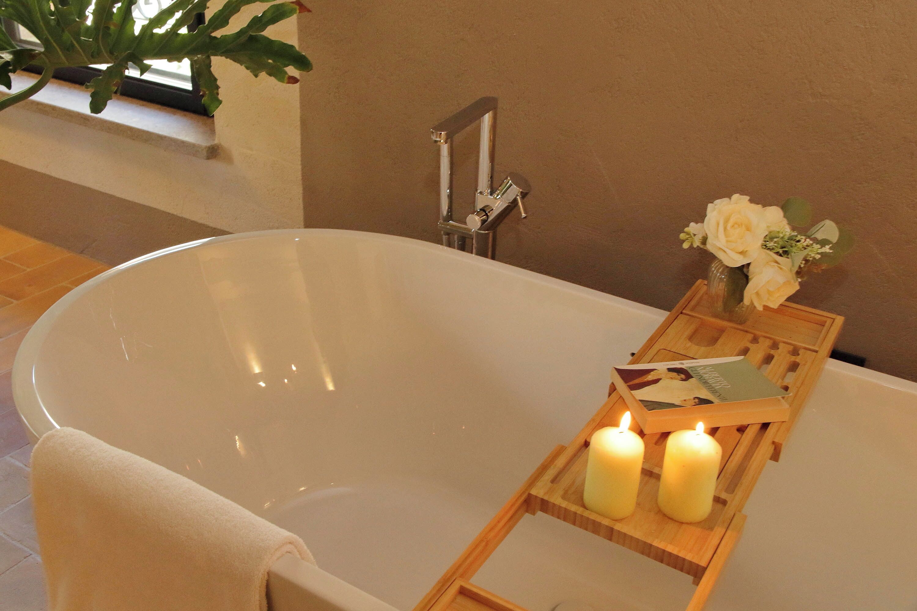 A bathtub with candles and a tray of books.