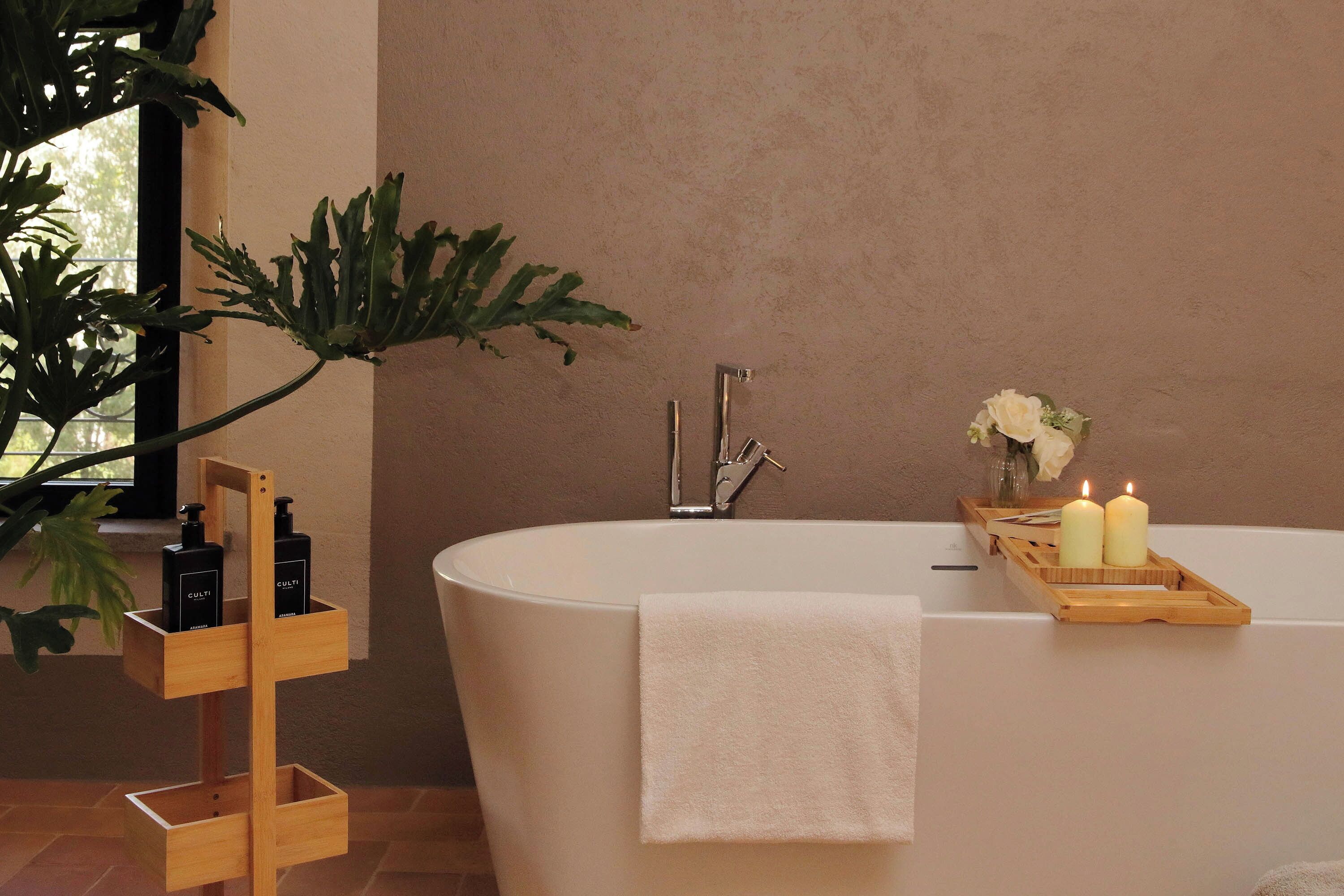 A bathroom with a freestanding wooden shelf holding toiletries, a bathtub with a towel, and candles.